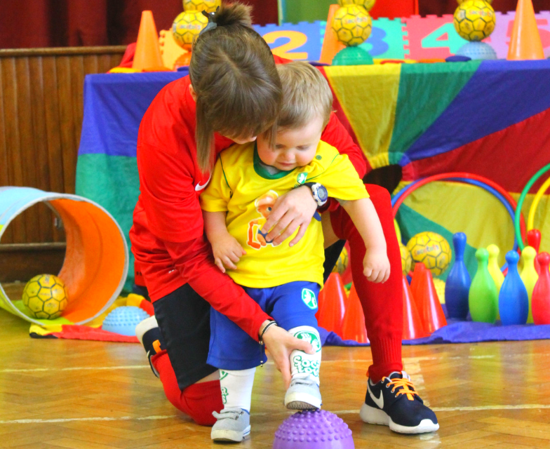 Football classes for Toddlers. Image shows SOCATOTS coach helping a toddler tap their foot onto a marker.