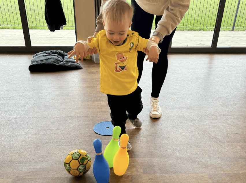 Toddlers first football class. Image shows a happy toddler kicking a ball into coloured cones in a Socatots class.