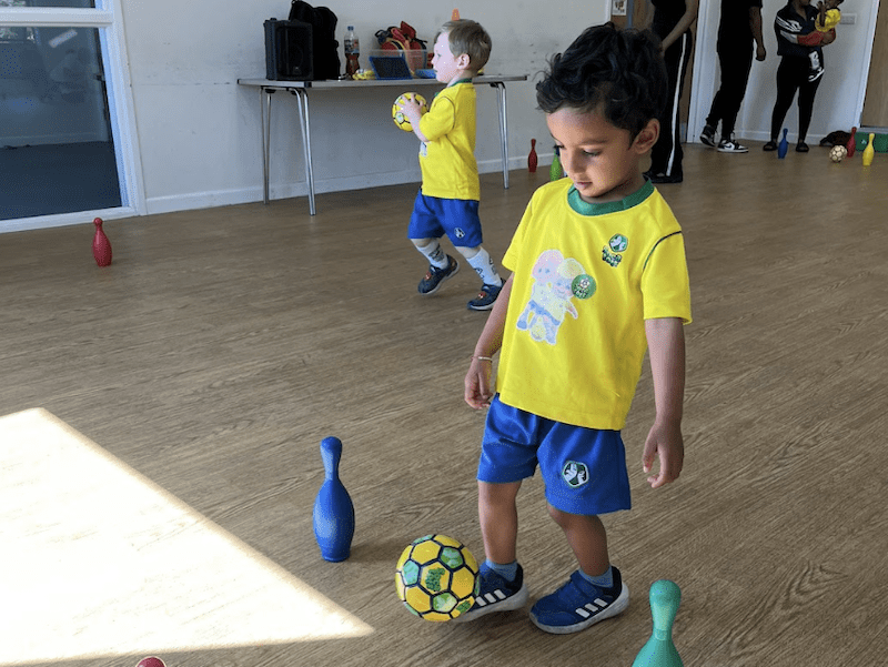 How to keep your toddler active. Image shows two toddlers in a socatots class, the nearest is kicking a football and the one in the background is running holding a socatots small football.