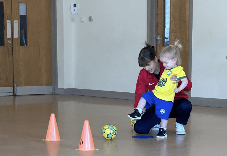 Is football safe for toddlers. Image shows a toddler in socatots kit kicking a small socatots football at a class.
