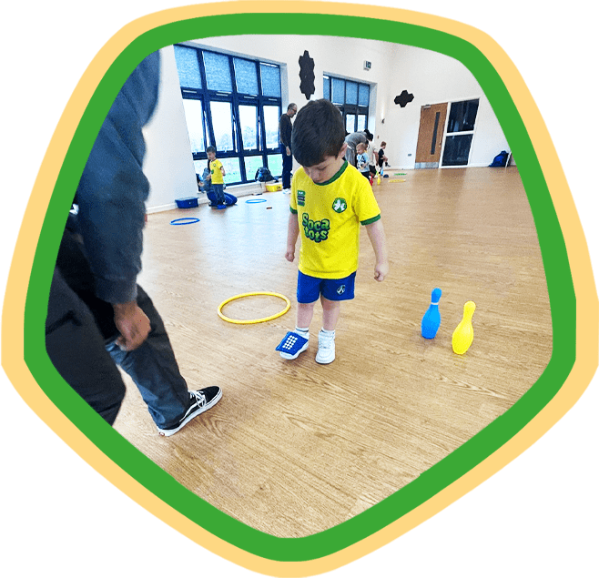 Image shows a child balancing a beanbag on his foot during a Socatots class
