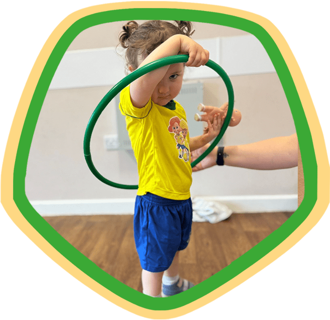 Image shows a toddler holding her plastic hoop over her head during a Socatots class