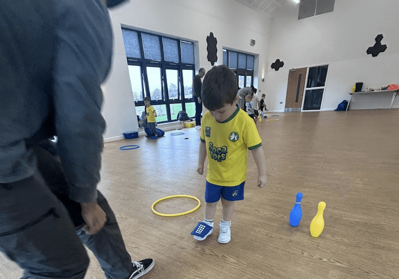 Toddler football classes in York. Image shows a father and son taking part in a Socatots class with the boy balancing a small bean bag on his foot.