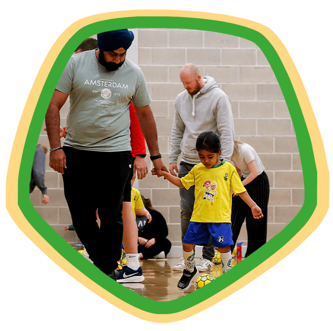 Father holding their toddler’s hand as they play football