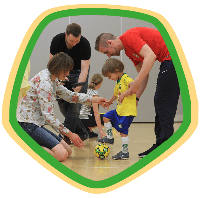 Toddler with a football being helped by their parent and our SOCATOTS coach