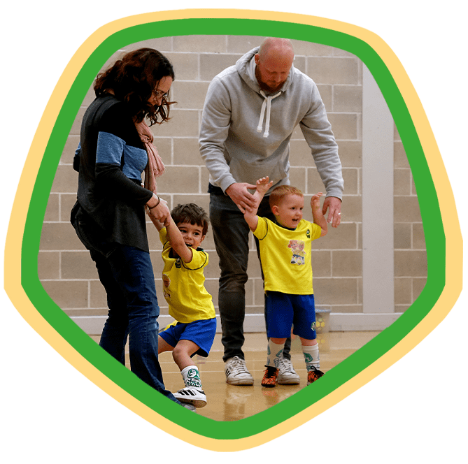 Two parents with their toddlers at a football training session