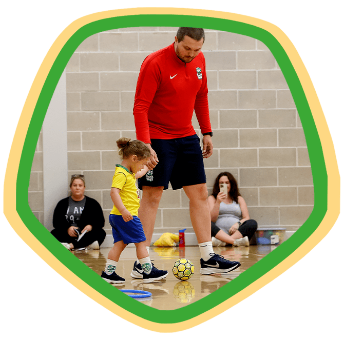 Young girl holding the hand of a SOCATOTS coach and kicking a football