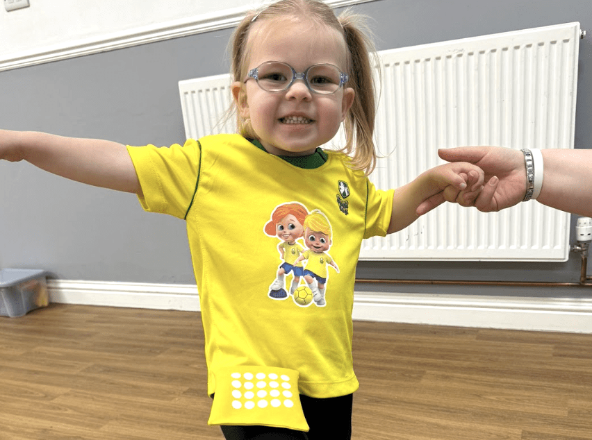 What age can kids start football training. Image shows a child balancing a beanbag on her leg in her Socatots uniform. 