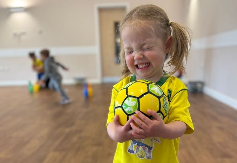Physical activities for toddlers. Image shows a toddler holding a socatots football smiling.