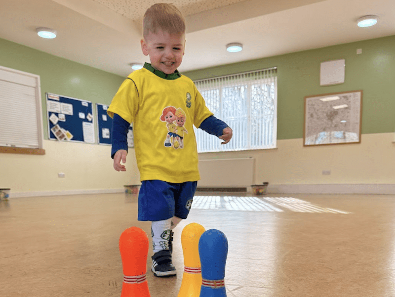 Toddler play ideas. Image shows toddler in football kit running towards skittles.