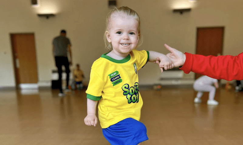 Best days out for toddlers. Image shows a toddler balancing whilst holding their parents hand during a Socatots class.