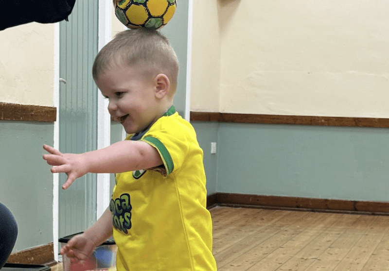 Toddler football classes in Bedford. Image shows a little boy in Socatots uniform balancing a Socatots baby football on his head.