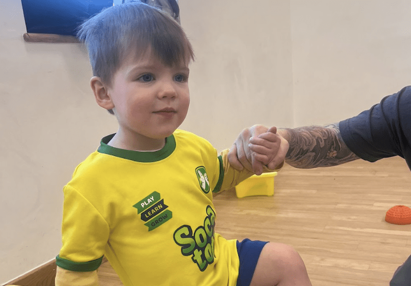Toddler football classes in Dunstable. Image shows a child holding hands with their parent and balancing during a Socatots class.