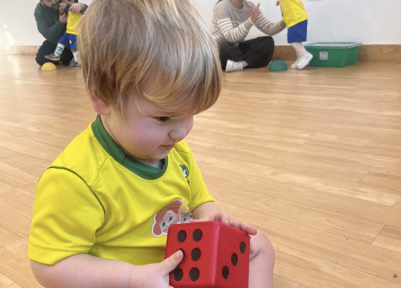 Toddler football club in Milton Keynes. Image shows a toddler holding a dice during a Socatots class in Socatots uniform. 