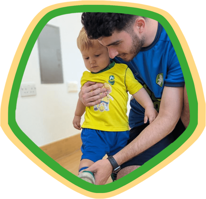 Image shows a Socatots coach helping a young toddler during a Socatots football class